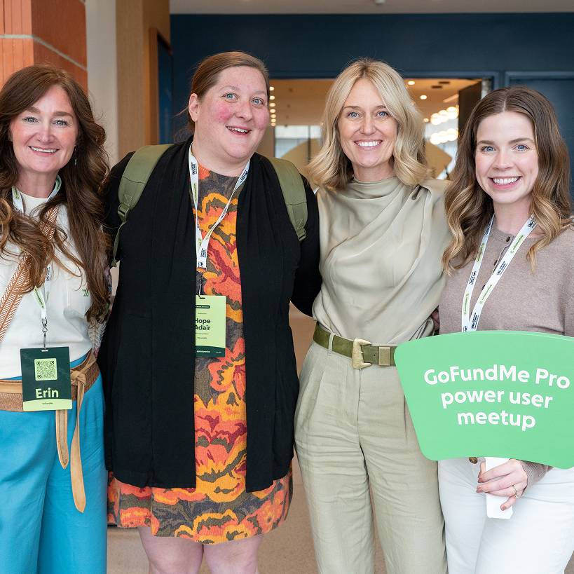 Four smiling women pose together at a GoFundMe Pro event, one holding a sign that reads 'GoFundMe Pro power user meetup'